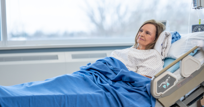 A senior woman lays back in her hospital bed with a neutral expression on her face as she recovers.